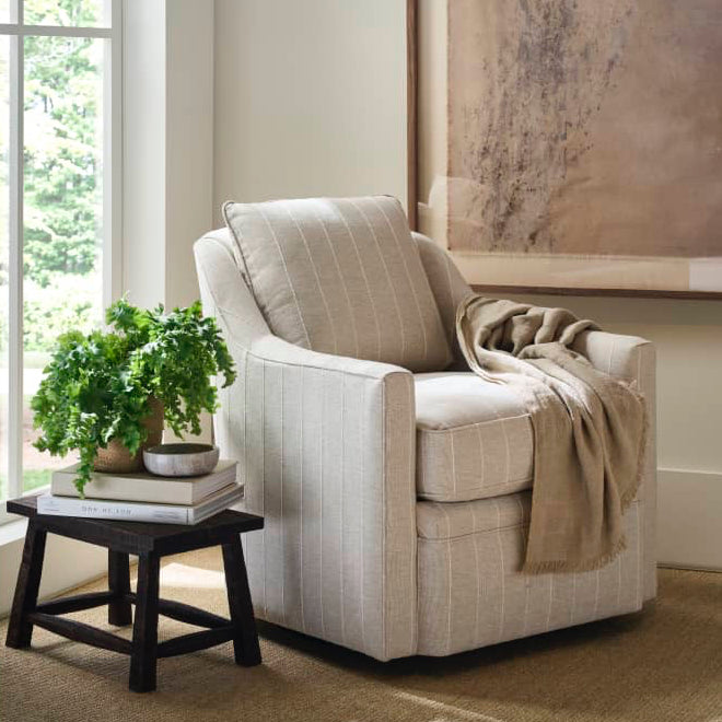Beige armchair in a room with a window, plant, and artwork.