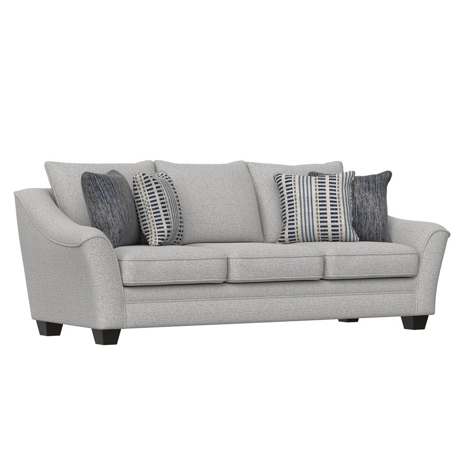 A light gray upholstered sofa with flared arms and welting detail, accompanied by a loveseat and chair, adorned with decorative pillows in blue and gray geometric prints and a textured stripe in navy.